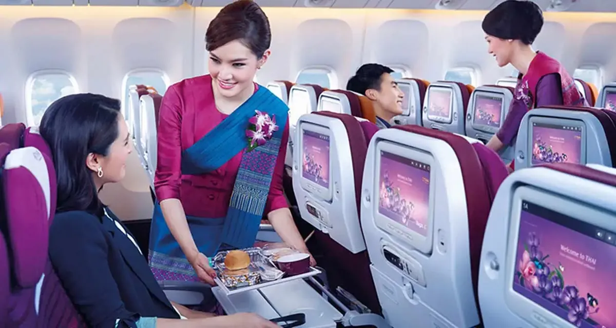 Thai Airways-ის ბორტგამცილებელი მგზავრს სადილის ლანგარს აწვდის, სავარძლებზე ეკრანები