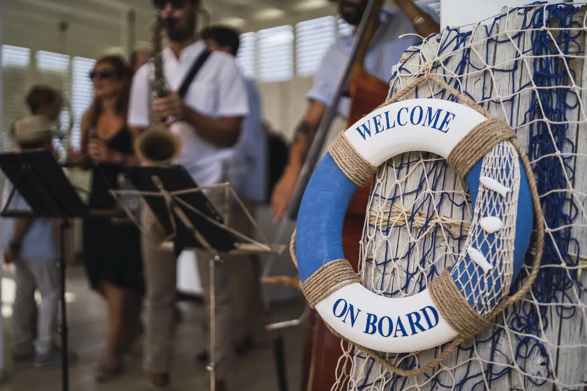 მუსიკოსები უკრავენ, წინ "Welcome on Board" წარწერიანი მაშველი რგოლი