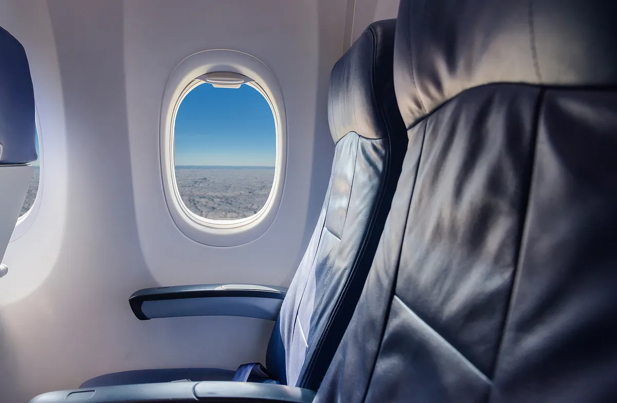 თვითმფრინავის ცარიელი ლურჯი სავარძლები და ილუმინატორი ცით